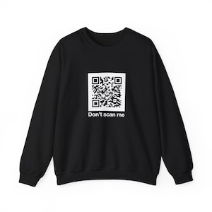 May include: A black long-sleeve sweatshirt featuring a white square graphic on the chest containing a black and white QR code. Below the QR code, the text "Don't scan me" is printed in a clean, white, sans-serif font.