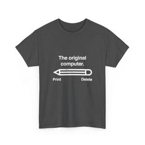 May include: A dark gray short-sleeve t-shirt featuring white text that reads The original computer. Below the text is a white graphic of a pencil with the word Print under the tip and the word Delete under the eraser end.