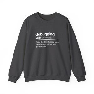 May include: A dark grey crewneck sweatshirt featuring white text that defines the word debugging as being the detective in a crime movie where you are also the murderer, complete with the verb label and phonetic pronunciation.
