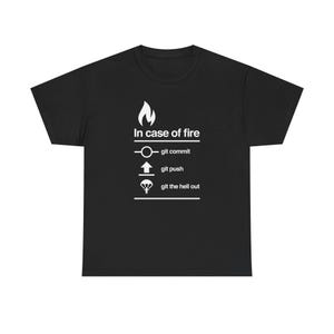Puede incluir: Camiseta negra con texto y gráficos blancos. El texto dice "In case of fire" sobre una serie de comandos: "git commit", "git push" y "git the hell out". El diseño incluye un icono de llama y otros símbolos.