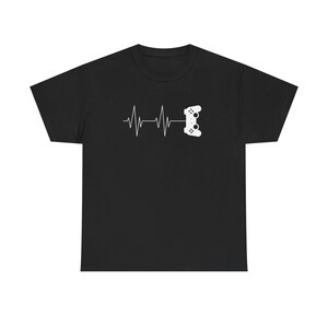 Puede incluir: Camiseta negra con un gráfico blanco. El diseño muestra una línea de latido del corazón que se transforma en un mando de videojuegos. El gráfico está centrado en el pecho. La camiseta es de material suave.