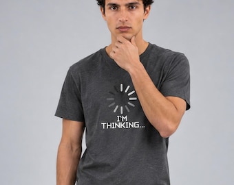 May include: A charcoal gray short-sleeved t-shirt featuring a white graphic of a circular loading icon above the text "I'M THINKING..." printed in a clean, sans-serif font centered on the chest of the garment.