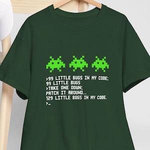 以下が含まれることがあります： ピクセル化された緑色のバグのデザインと「99 Little Bugs in My Code」のテキストが入った濃い緑色のTシャツ。 シャツはクルーネックと半袖です。 面白いグラフィックTシャツです。