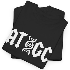 Op de afbeelding: Twee zwarte t-shirts zijn opgevouwen en op elkaar gestapeld. Het bovenste shirt heeft de witte tekst "ATGC" in een vet, gotisch lettertype, met een DNA-dubbele helix-symbool. De shirts zijn gemaakt van een zacht materiaal.