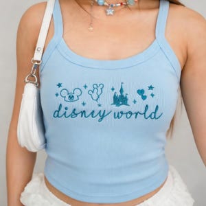 Peut inclure: D&eacute;bardeur c&ocirc;tel&eacute; bleu clair avec un motif Disney World brod&eacute; en bleu plus fonc&eacute;. Le motif comprend Mickey Mouse, des ballons, un ch&acirc;teau et des &eacute;toiles. Le d&eacute;bardeur a une encolure d&eacute;gag&eacute;e et de fines bretelles.