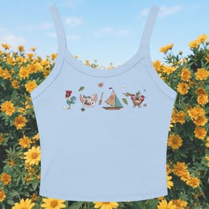 K&ouml;nnte beinhalten: Hellblaues Tanktop mit einer Reihe von Cartoon-Charakter-Illustrationen. Die Illustrationen zeigen einen Hahn, ein Schwein, ein Boot und eine Frucht. Das Tanktop hat d&uuml;nne Tr&auml;ger und einen Rundhalsausschnitt.