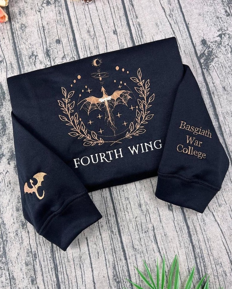 May include: Black sweatshirt with gold dragon and text. The front displays a dragon design with "FOURTH WING". The right sleeve has "Basgiath War College" and the left sleeve has a dragon emblem.