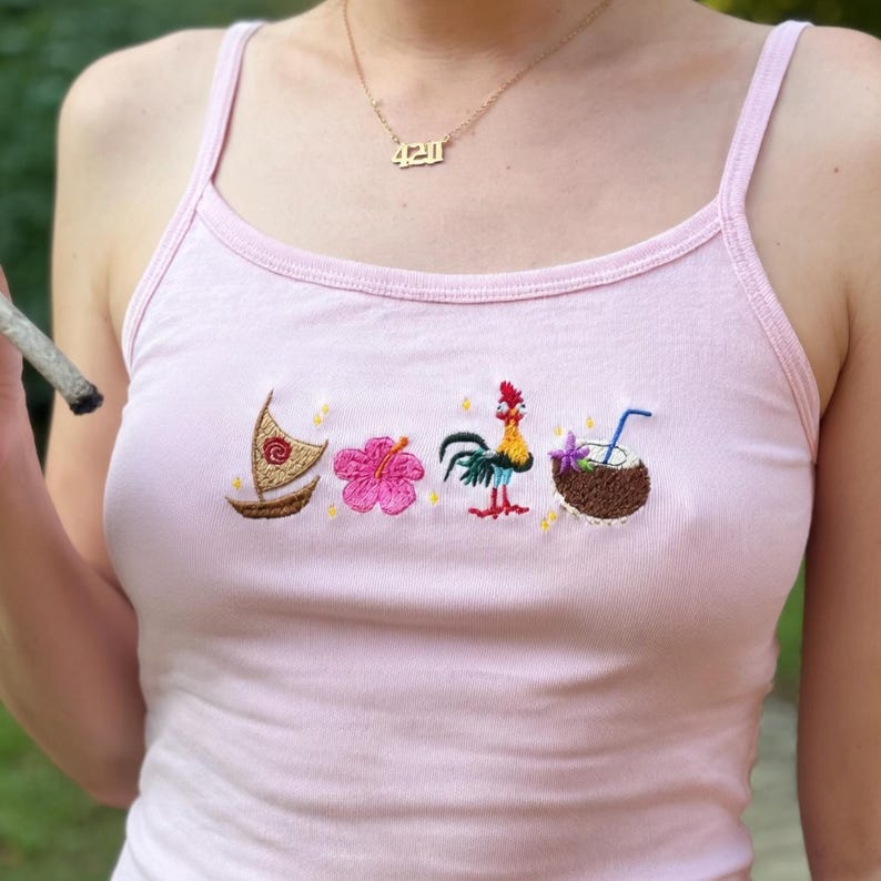 May include: Pink tank top with embroidered tropical designs, including a sailboat, hibiscus flower, rooster, and coconut drink. A gold necklace with the number "420" is visible. The tank top has thin straps.