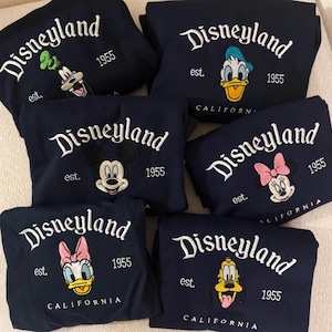 Peut inclure: Des sweat-shirts bleu marine avec des broderies "Disneyland" et des personnages. Chaque sweat-shirt pr&eacute;sente un personnage Disney diff&eacute;rent : Dingo, Donald Duck, Mickey Mouse, Minnie Mouse, Daisy Duck et Pluto. "est. 1955" et "CALIFORNIA" sont &eacute;galement brod&eacute;s.