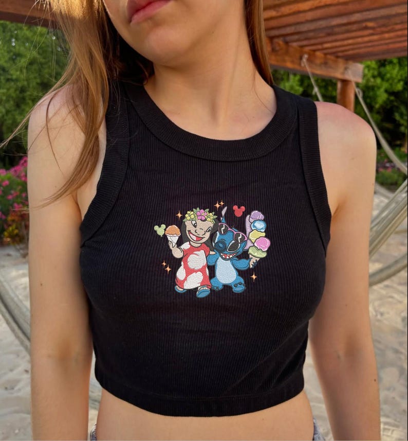 May include: Black ribbed tank top with a colorful embroidered graphic featuring two cartoon characters holding ice cream cones. The graphic includes a character in a red dress and a blue character, both with floral accents.