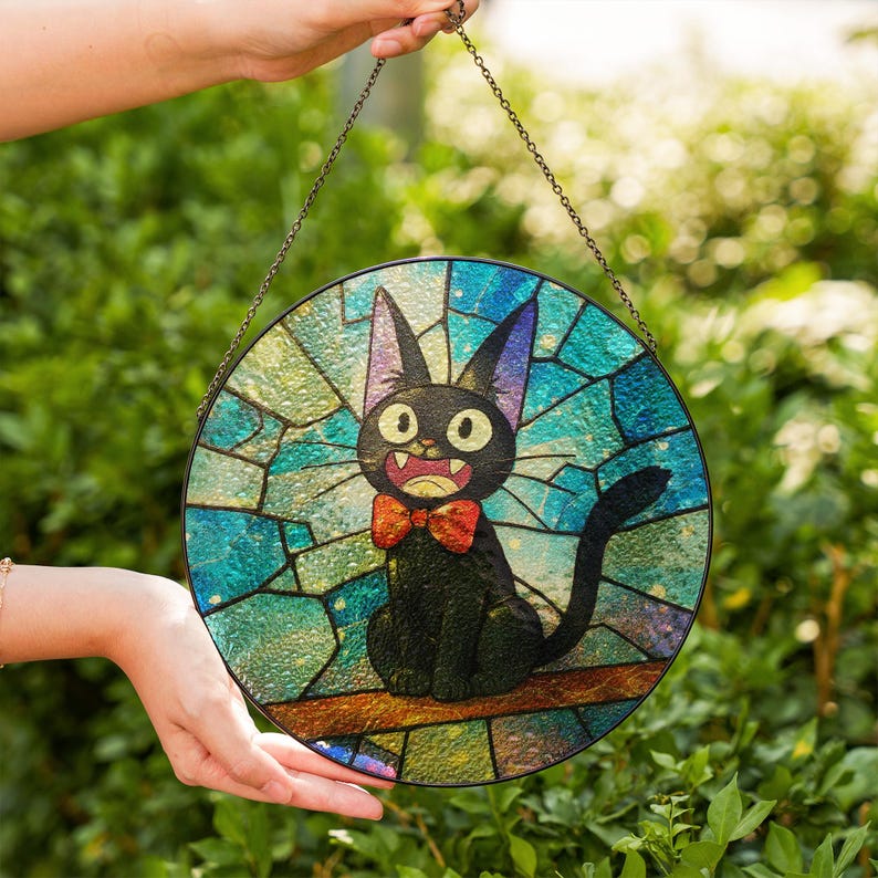 May include: Round stained glass panel featuring a black cat with a red bow tie, set against a blue and green background. The cat has large yellow eyes and is perched on a brown branch. The panel is held by a chain.