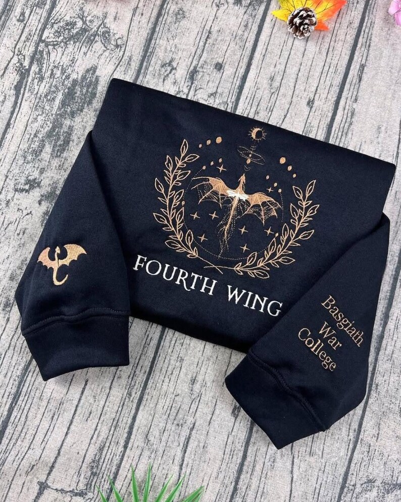 May include: Black sweatshirt with gold dragon and text. The front displays a dragon design within a laurel wreath and the words "FOURTH WING." The left sleeve has a dragon emblem, and the right sleeve says "Basgiath War College."
