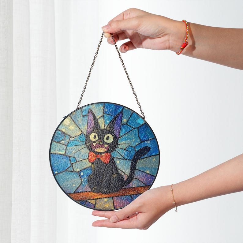 May include: Round stained glass panel featuring a black cat with a red bow tie, set against a blue and gold mosaic background. The cat is perched on a brown branch, suspended by a metal chain.