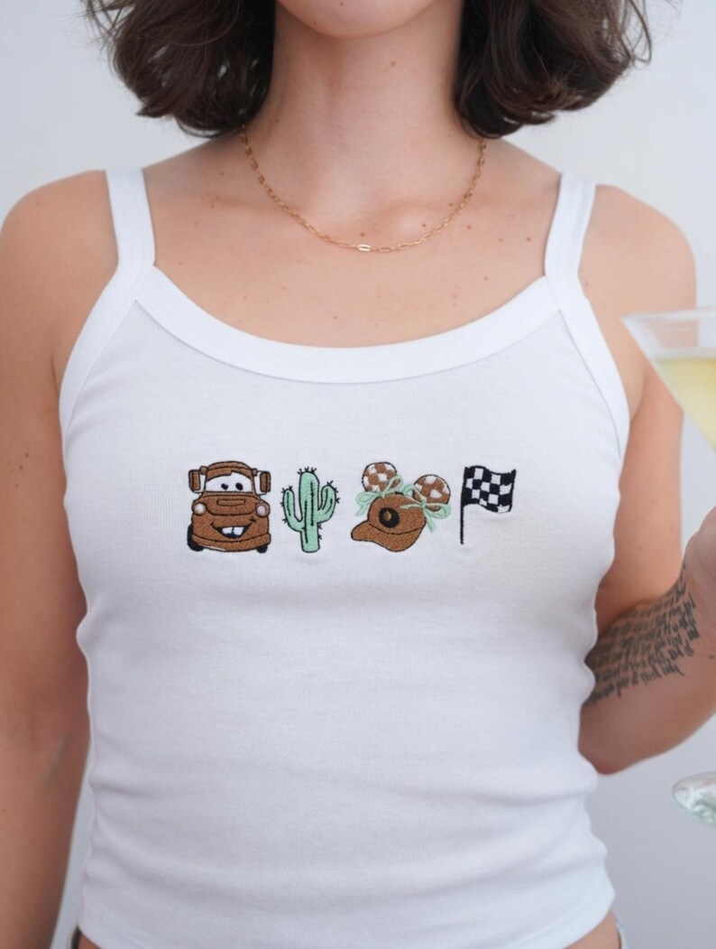 May include: A white tank top featuring a horizontal row of four embroidered designs: a brown tow truck, a light green cactus, a brown baseball cap with mouse ears and a light green bow, and a black and white checkered racing flag.