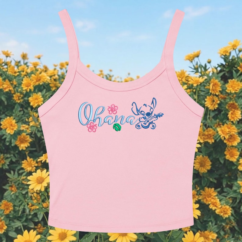 May include: Pink tank top with the word "Ohana" in blue script, along with a cartoon character playing a ukulele. The top has thin straps and is set against a backdrop of yellow flowers and a blue sky.