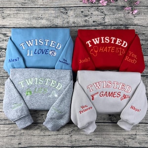 May include: Four sweatshirts in blue, red, gray, and white, each embroidered with the word "TWISTED." The blue sweatshirt says "LOVE" with a camera icon. The red sweatshirt says "HATE" with a stethoscope icon. The gray sweatshirt says "LIES" with a lock icon. The white sweatshirt says "GAMES" with a gun icon.