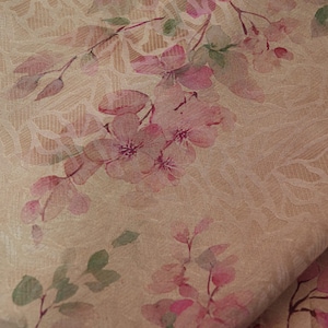 May include: Close-up of a fabric with a floral pattern. The design features pink flowers and green leaves on a beige background. The fabric has a textured appearance, with subtle lines and patterns adding depth to the design. The overall aesthetic is soft and delicate.