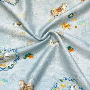 May include: Light blue fabric with a repeating pattern of horses, clouds, and gold ingots. The horses are adorned with colorful saddles and bridles. The fabric has a subtle, textured appearance.