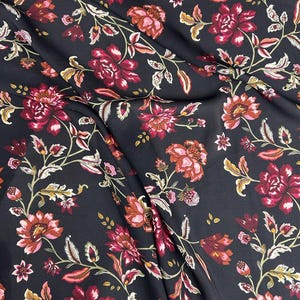 Pode incluir: Tecido escuro com um padrão floral. O design apresenta grandes flores vibrantes em tons de vermelho, rosa e pêssego, com folhas e caules verdes e dourados, sobre um fundo preto.