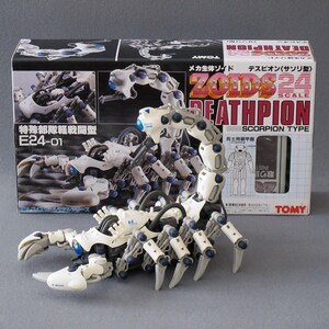 May include: A white and gray plastic toy robot in the shape of a scorpion. The robot is called "Deathpion" and is a "Scorpion Type" from the "Zoids" toy line. The box is labeled "1/24 Scale".
