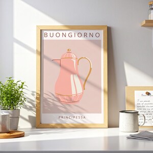 Könnte beinhalten: Ein gerahmter Kunstdruck mit einer rosa Kaffeekannen-Illustration und goldenen Akzenten. Die italienischen Wörter "Buongiorno" und "Principessa" sind auf dem Kunstwerk abgebildet. Der Druck steht auf einer weißen Arbeitsplatte mit Pflanzen und einer Tasse.