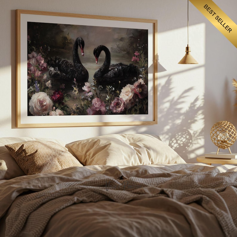 May include: A framed art print featuring two black swans amidst pink and white flowers. The artwork has a vintage aesthetic, with a wooden frame and a "Best Seller" banner in the upper right corner. The print is displayed above a bed with neutral-toned bedding.