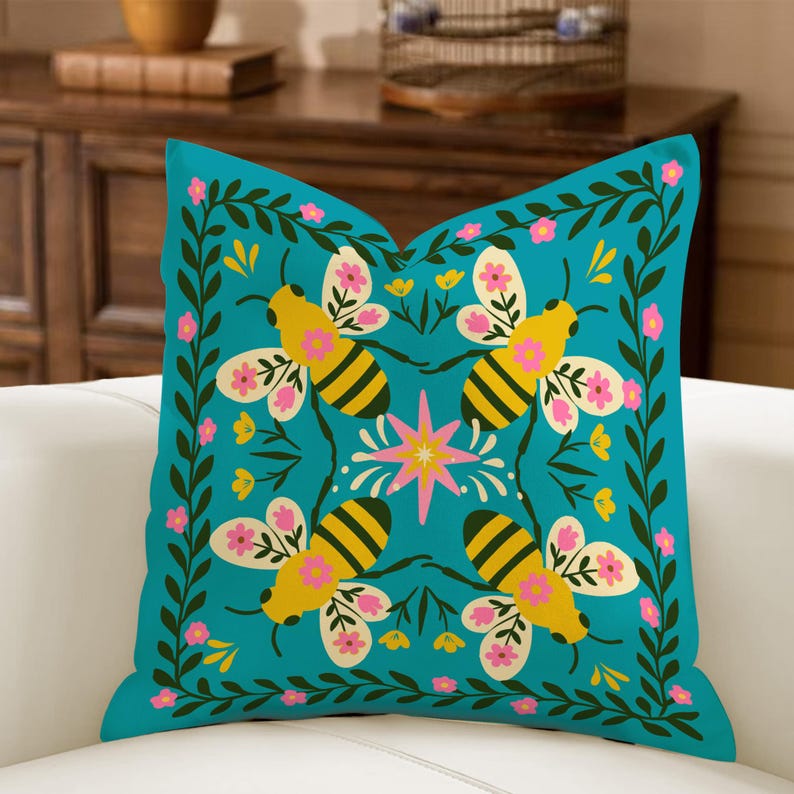 May include: Square teal throw pillow with a repeating pattern of yellow and black bees, pink flowers, and green foliage. The bees are centered around a pink and yellow starburst design. The pillow is on a white surface.
