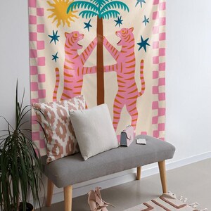 Puede incluir: Un tapiz decorativo con un dise&ntilde;o caprichoso. Presenta dos tigres rosas abrazando un &aacute;rbol, un sol amarillo y estrellas azules. El tapiz tiene un borde a cuadros rosa y blanco. Debajo, un banco gris con cojines, zapatos y una alfombra.