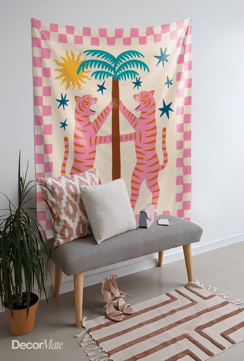 Puede incluir: Un tapiz decorativo con un dise&ntilde;o caprichoso. Presenta dos tigres rosas abrazando un &aacute;rbol, un sol amarillo y estrellas azules. El tapiz tiene un borde a cuadros rosa y blanco. Debajo, un banco gris con cojines, zapatos y una alfombra.