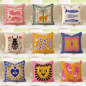 May include: A selection of decorative cushions with diverse designs. Cushions feature colourful illustrations of tigers, fish, a leopard, a beetle, a snake, a lion, and an eye. The cushions are square and made of fabric.