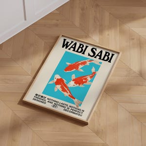 May include: A framed art print featuring the words "WABI SABI" in black above three koi fish illustrations. The fish are red and white against a light blue background. The print also includes Japanese text and the phrase "NOTHING LASTS, NOTHING IS FINISHED, AND NOTHING IS PERFECT."