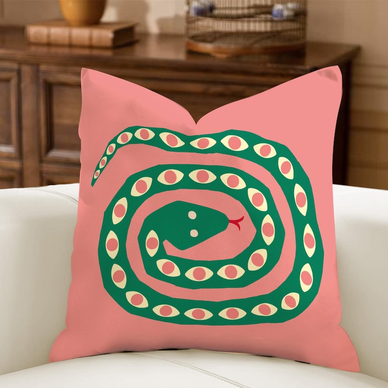 May include: A cushion with a pink background and a green snake design. The snake is coiled and has multiple eye-shaped details in cream with pink centres. The snake's tongue is red.
