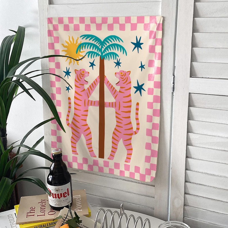 Puede incluir: Un tapiz decorativo con un dise&ntilde;o caprichoso. Presenta dos tigres rosas flanqueando una palmera. El fondo tiene un patr&oacute;n de cuadros rosas y blancos, con un sol amarillo y estrellas azules.