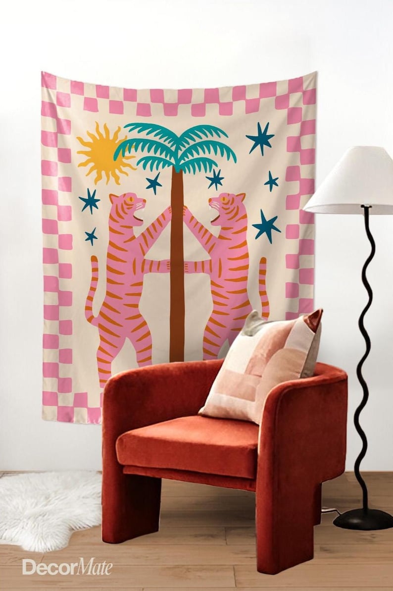 Puede incluir: Un tapiz de pared decorativo con un dise&ntilde;o caprichoso con dos tigres rosas abrazando una palmera. El tapiz tiene un fondo crema con un borde a cuadros rosa, un sol amarillo y estrellas azules. Sobre una silla roja.