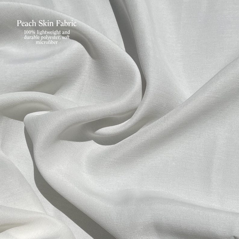 May include: Close-up of white peach skin fabric with soft, flowing folds. The fabric is 100% lightweight and durable polyester microfiber. The text "Peach Skin Fabric" is visible in the upper left corner.