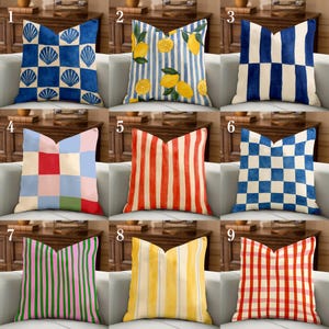 Può includere: Nove cuscini decorativi con vari motivi sono esposti su un divano bianco. I motivi includono conchiglie, limoni, strisce e motivi a scacchi in colori come blu, rosso, rosa e giallo. I cuscini sono quadrati e aggiungono un tocco decorativo a qualsiasi spazio abitativo.