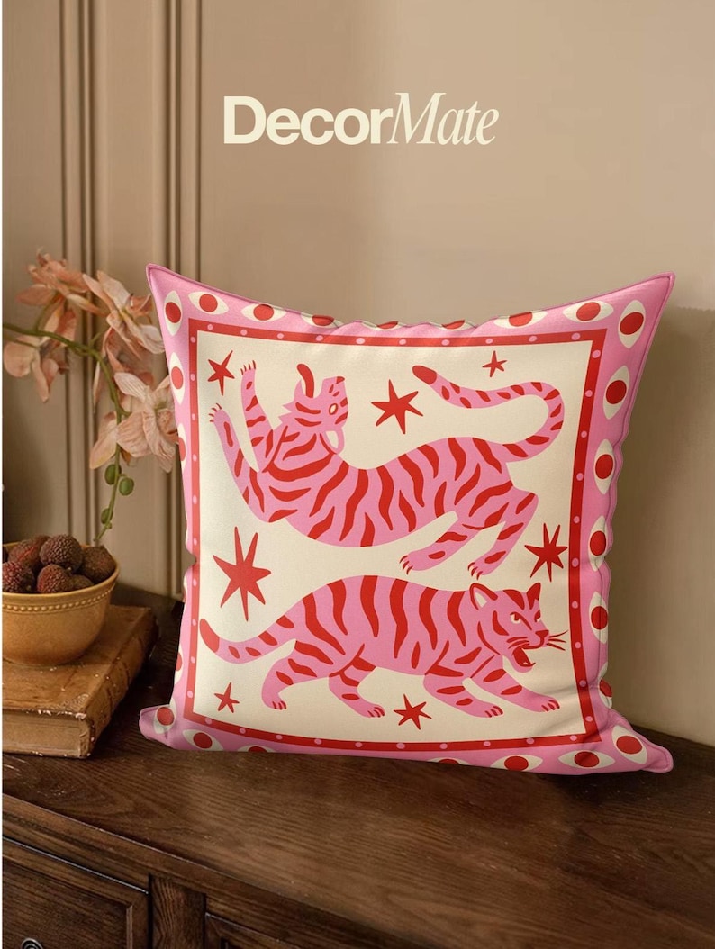 May include: Pink decorative pillow featuring two stylized tigers with red stripes and stars on a cream background. The pillow has a pink border with red circles and the text "DecorMate" at the top.