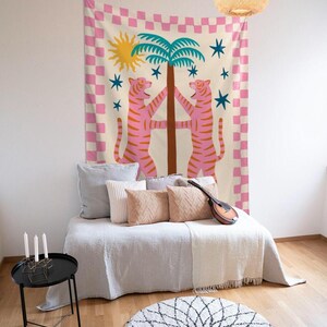 Puede incluir: Un tapiz decorativo con un dise&ntilde;o caprichoso. Dos tigres rosas abrazan una palmera, sobre un fondo crema con un borde a cuadros rosa y blanco. Estrellas azules y un sol amarillo completan el dise&ntilde;o.