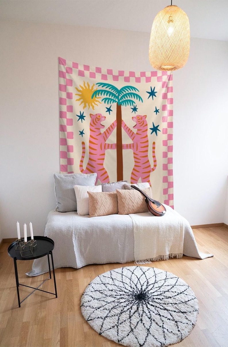 Puede incluir: Un tapiz decorativo con un dise&ntilde;o caprichoso. Dos tigres rosas abrazan una palmera, sobre un fondo crema con un borde a cuadros rosa y blanco. Estrellas azules y un sol amarillo completan el dise&ntilde;o.