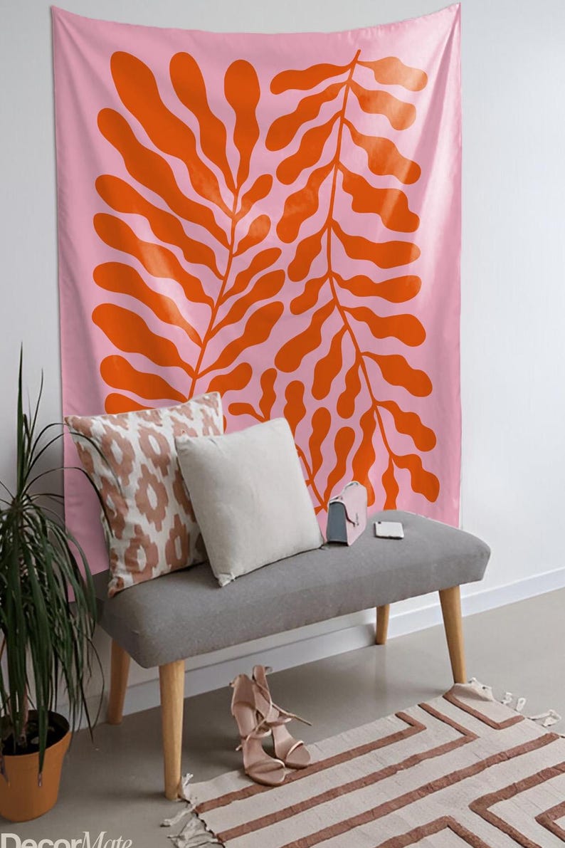 May include: A pink wall tapestry with a large orange leaf design hangs above a gray bench with pillows and a small purse. A potted plant and a rug with a geometric pattern are in the foreground. The scene is a modern interior.