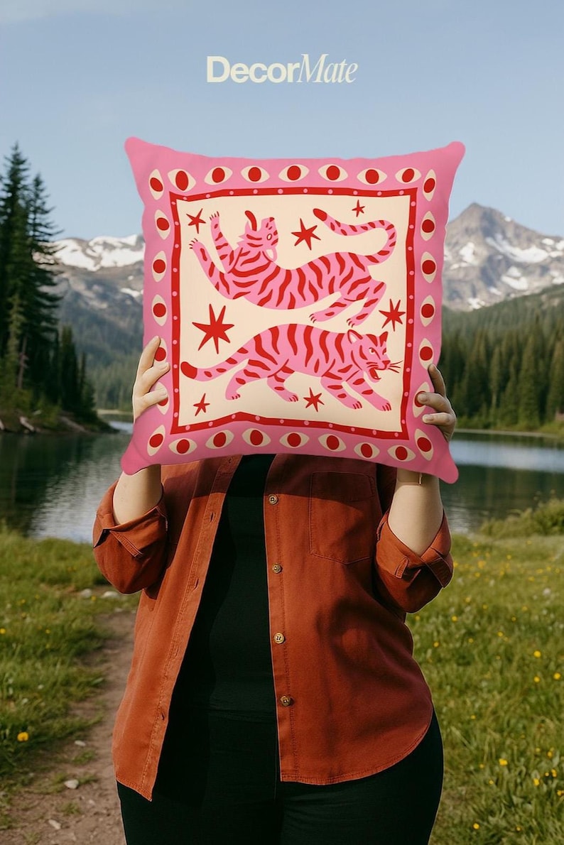 May include: Pink decorative pillow with a cream-colored center featuring two pink striped tigers and red star accents. The pillow has a pink border with red eye and dot designs. The text "DecorMate" is at the top.