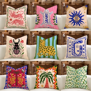 May include: Collection of decorative throw pillows with various designs. Pillows feature a pink tiger, a pink leopard with "HOWDY" text, a blue eye, a black beetle, a yellow leopard, a blue face, a red snake, a palm tree, and a green leopard print.