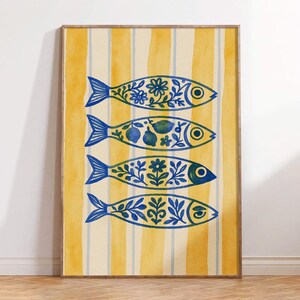 May include: A framed art print featuring four stylized fish with blue floral and fruit patterns. The fish are set against a yellow and white striped background. The artwork is framed in a light brown wooden frame.