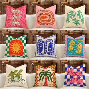 Könnte beinhalten: Eine Sammlung von neun dekorativen Wurfkissen mit verschiedenen farbenfrohen Designs. Die Kissen zeigen Muster wie Leoparden, Schlangen, Sonnen, Gesichter, Dinosaurier, Palmen und Tiger. Jedes Kissen hat ein einzigartiges Design und Farbschema.