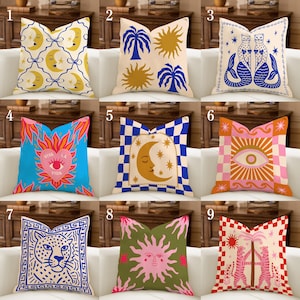 May include: Nine decorative throw pillows with various designs are displayed. The pillows feature celestial, animal, and geometric patterns in colors like blue, yellow, pink, and green. The designs include moons, suns, palm trees, mermaids, and a leopard.