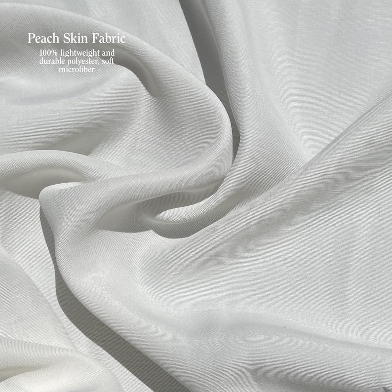 Puede incluir: Primer plano de tela blanca de piel de melocot&oacute;n. La tela es 100% poli&eacute;ster ligero y duradero, microfibra suave. La tela est&aacute; drapeada en pliegues suaves, creando sombras y reflejos. El texto "Peach Skin Fabric" es visible en la esquina superior izquierda.