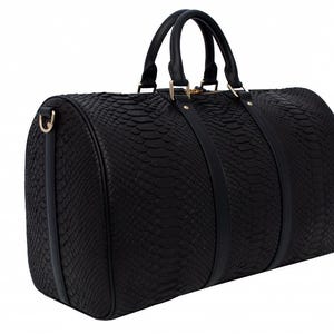 May include: A black leather travel bag with a snakeskin pattern. The bag has two top handles and a shoulder strap.