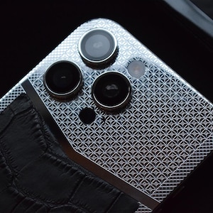May include: A silver smartphone with a geometric pattern on the back. The phone has a black leather case with a crocodile pattern. The phone has four cameras on the back.