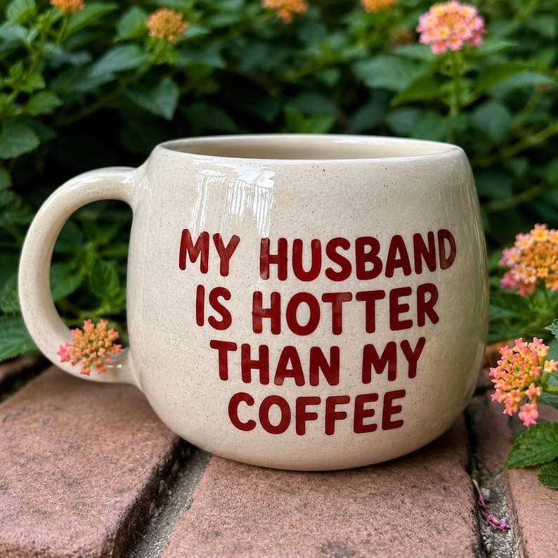 Puede incluir: Taza de cer&aacute;mica color crema con forma redondeada y asa grande. La taza presenta el texto "MY HUSBAND IS HOTTER THAN MY COFFEE" en letras rojas. Ideal para caf&eacute; o t&eacute;.