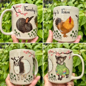 May include: Cream-colored ceramic mugs with animal illustrations. One mug features a rabbit, another a rooster, a goat, and a dog in a green sweater. Each mug has the text "Frenchy's" or "Frenchy's Farm" and floral accents.